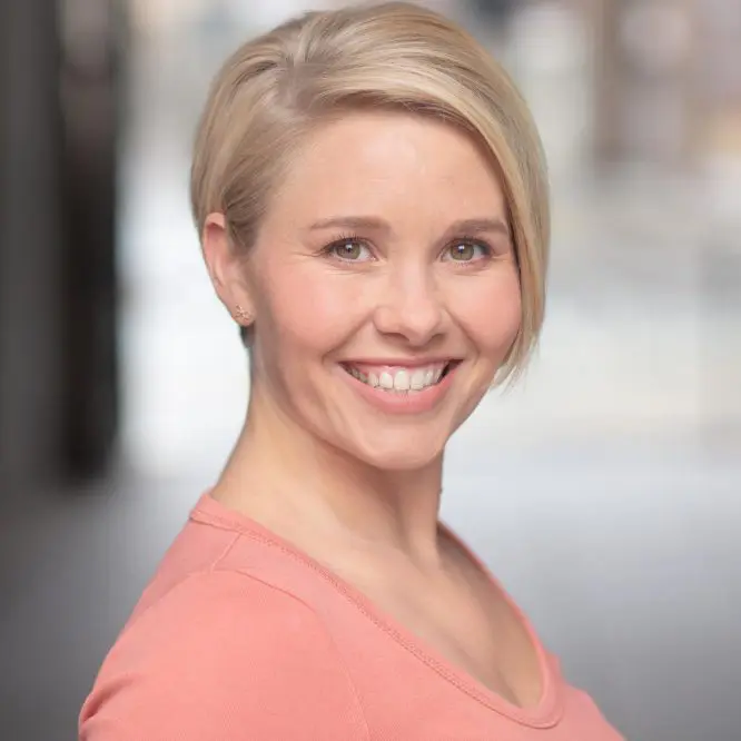 LinkedIn corporate headshot of a smiling woman in a coral top