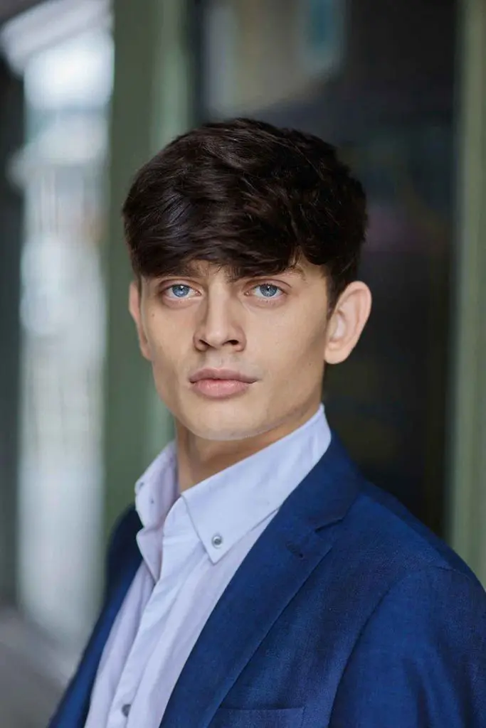 Corporate headshot of a young man in a navy blazer photographed outdoors
