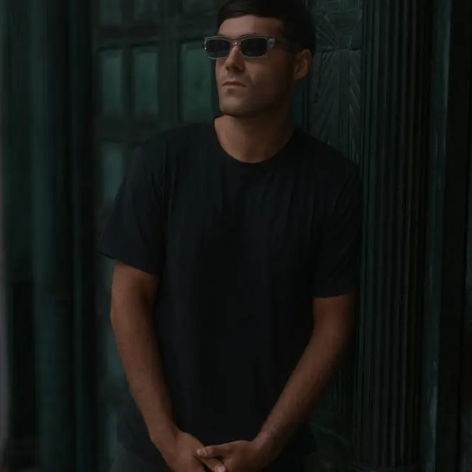 DJ in sunglasses standing in a dark green doorway for a press shot