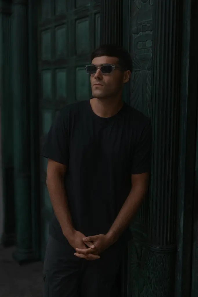 DJ in sunglasses standing in a dark green doorway for a press shot