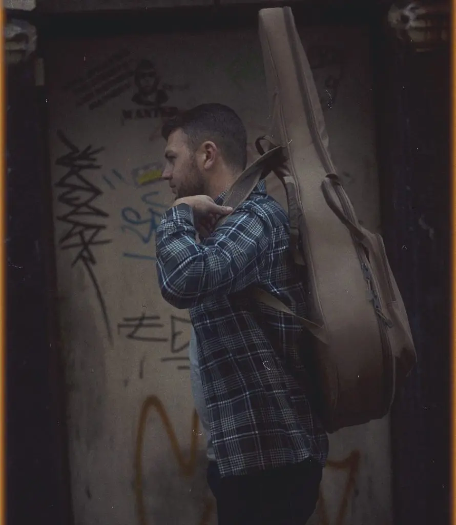Musician carrying a guitar case beside a graffitied metal shutter