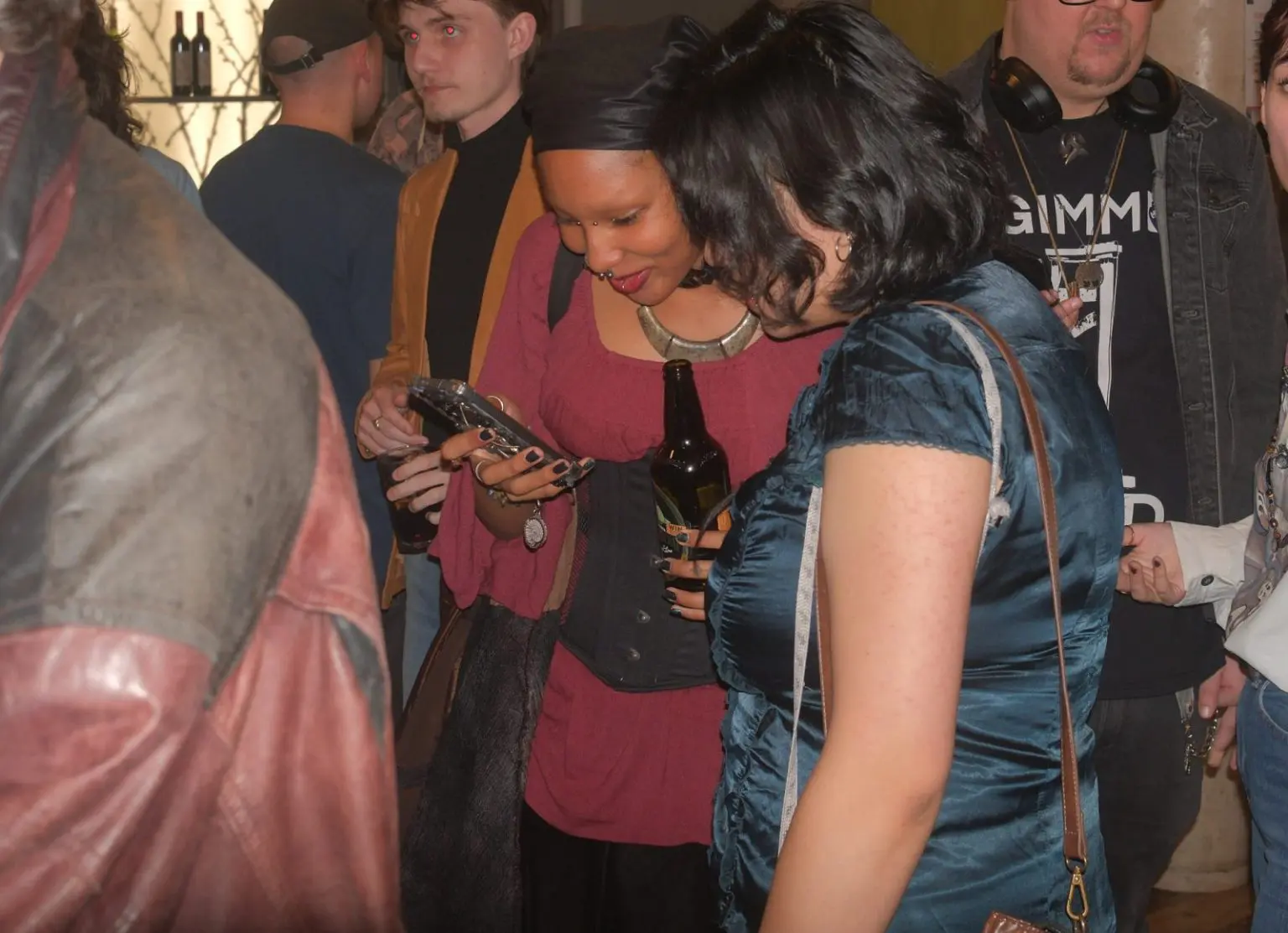 Guests sharing a phone and drinks in a packed room at a creative industry social mixer in Liverpool