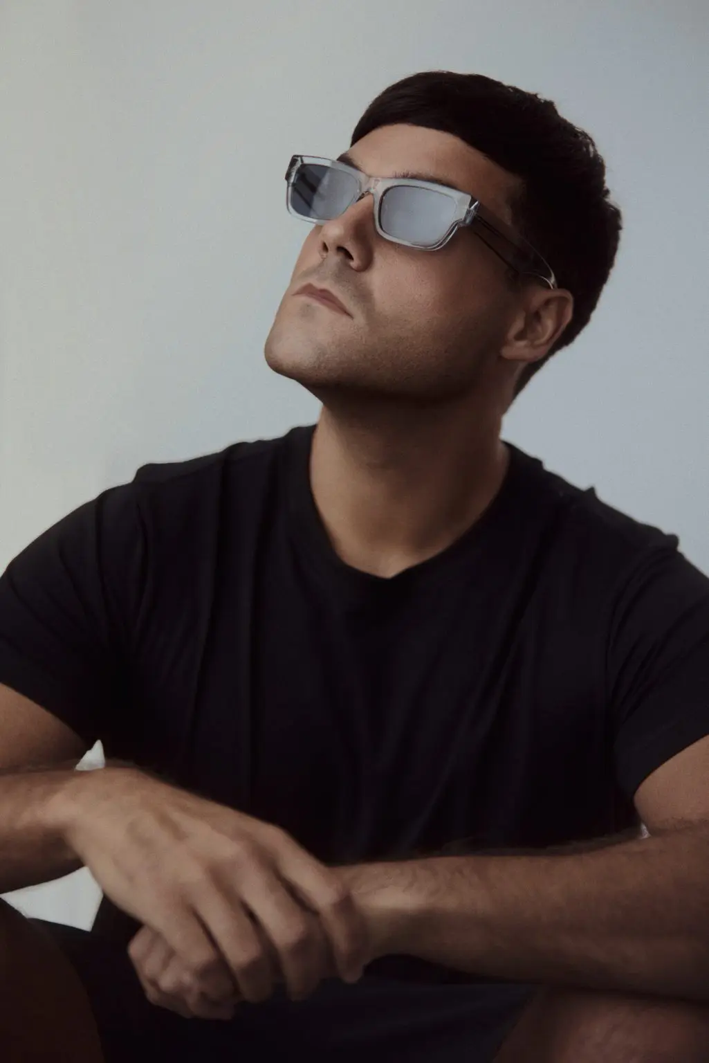 Music artist in sunglasses and a black t-shirt seated against a soft grey backdrop