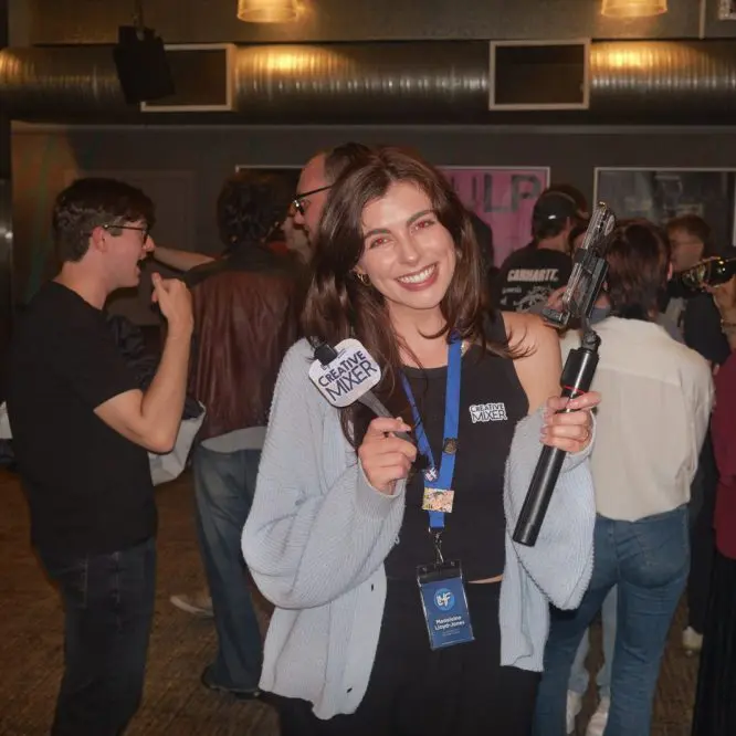 Smiling host holding a Creative Mixer microphone and phone gimbal among guests at the Let's Make Films social mixer, FACT Picture House Liverpool
