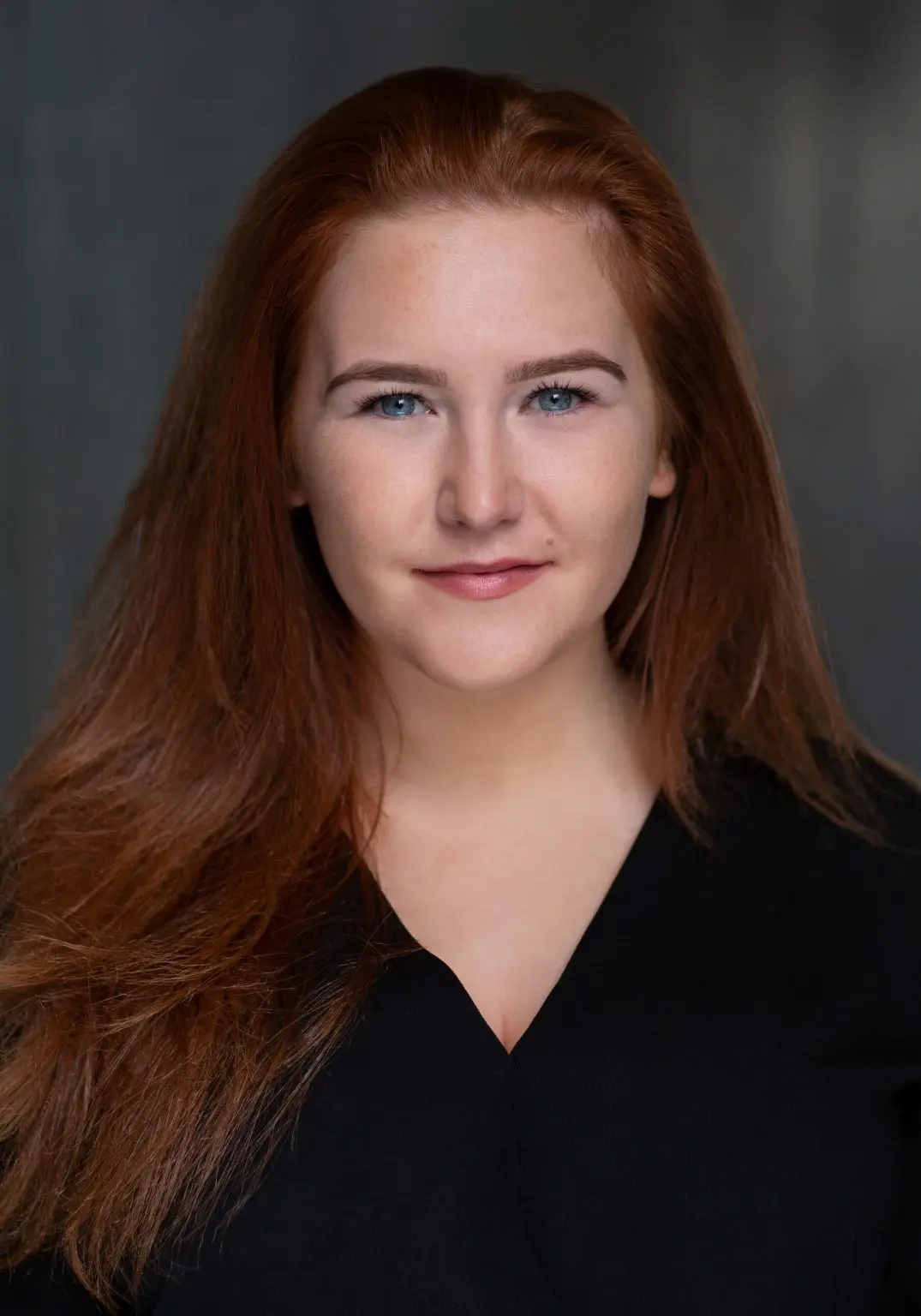 Headshot of a red-haired actress in a black shirt against a dark background