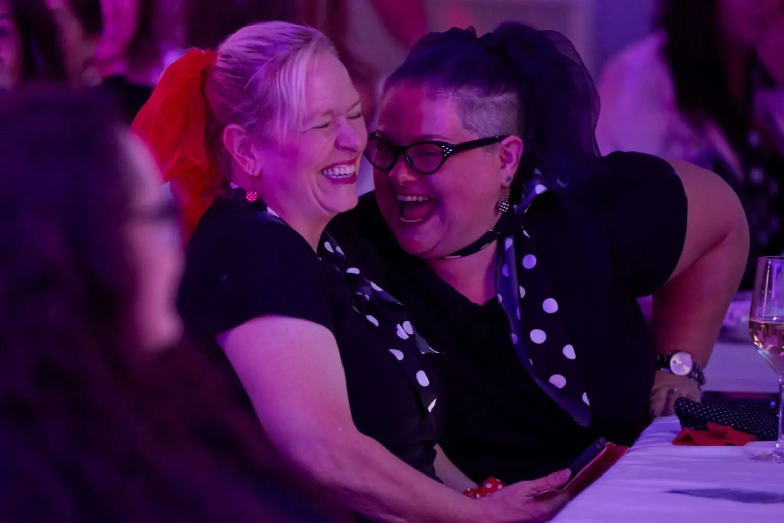 Two guests in polka dot scarves laughing together at their table during a themed bottomless brunch event in Liverpool, candid event photography