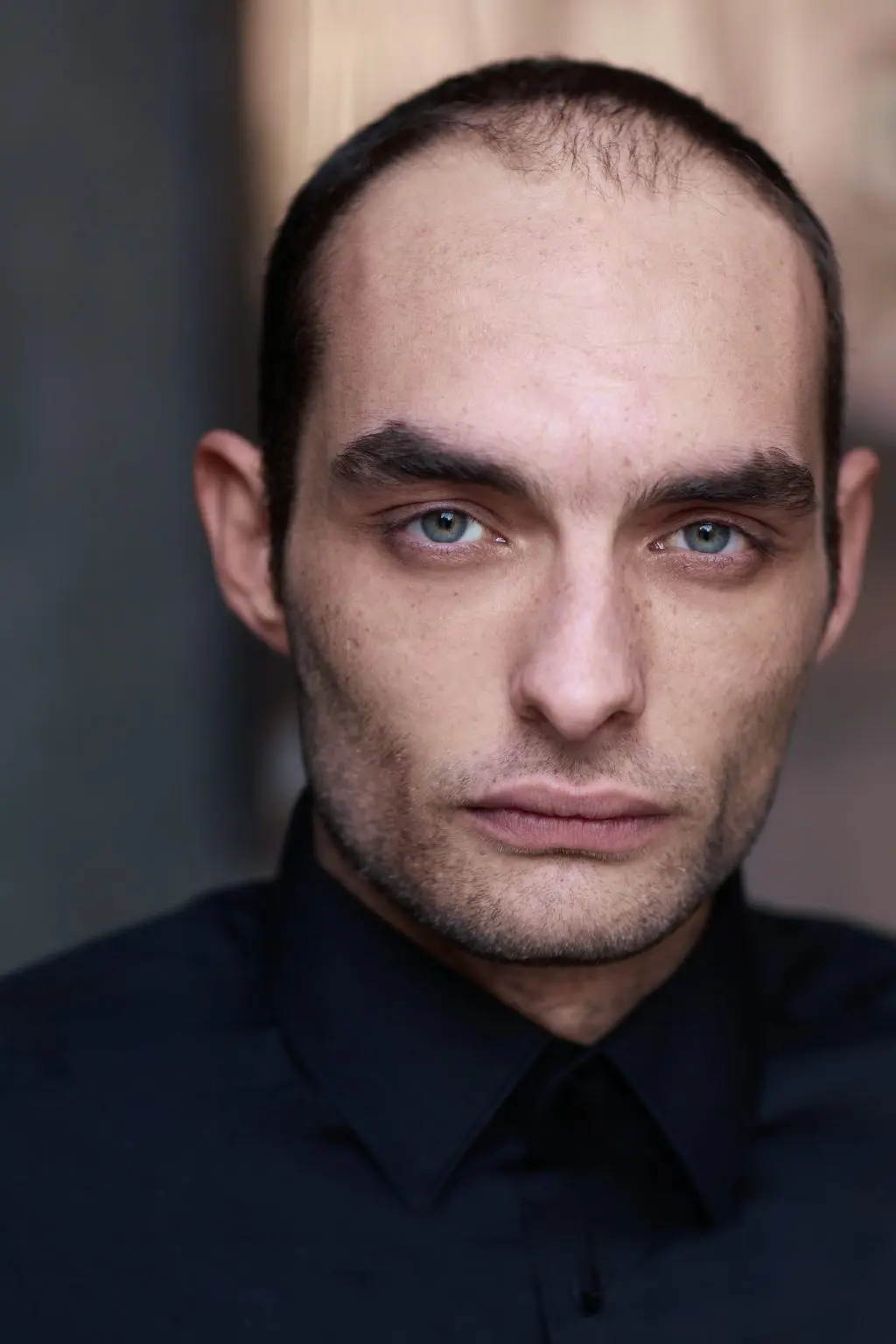 Cinematic actor headshot of a man in a dark shirt against a shadowed wall