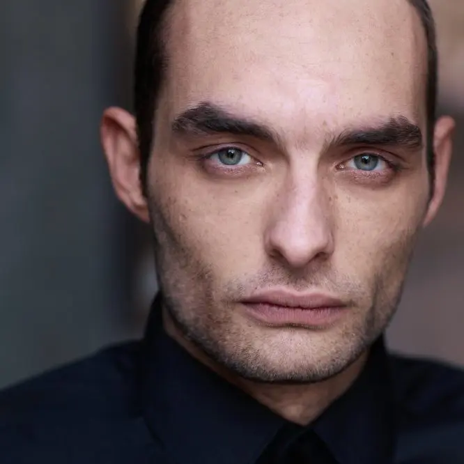 Cinematic actor headshot of a man in a dark shirt against a shadowed wall