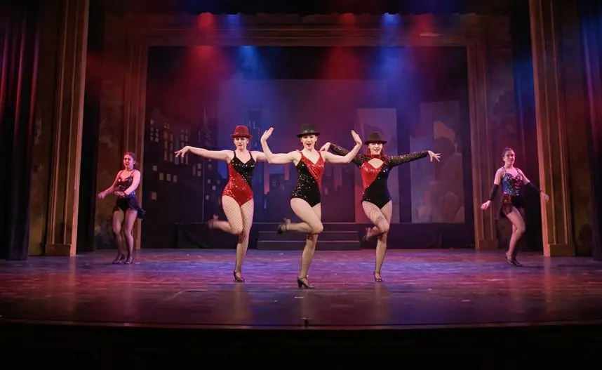 Dancers in cabaret costume performing under red and blue stage lighting