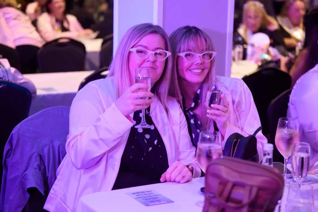 Two friends in matching retro glasses raising a toast with prosecco at a Grease themed bottomless brunch in Liverpool