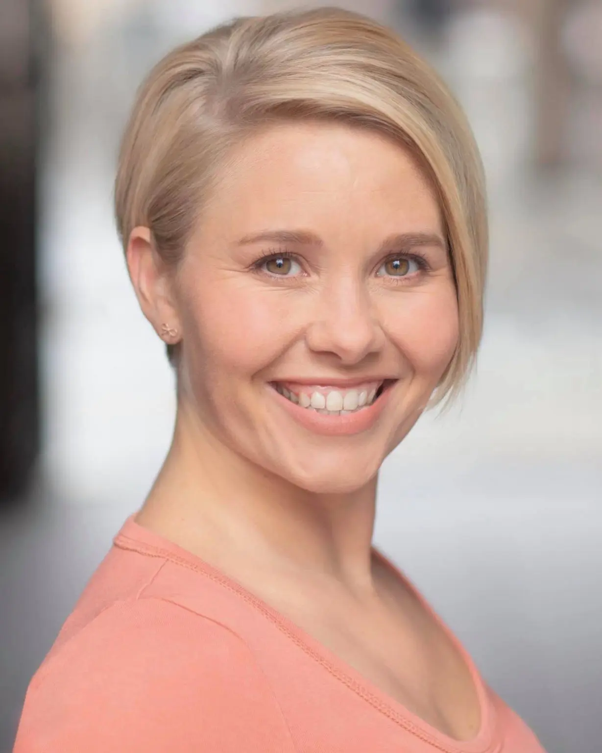 Commercial casting headshot of a smiling blonde actress in a coral top