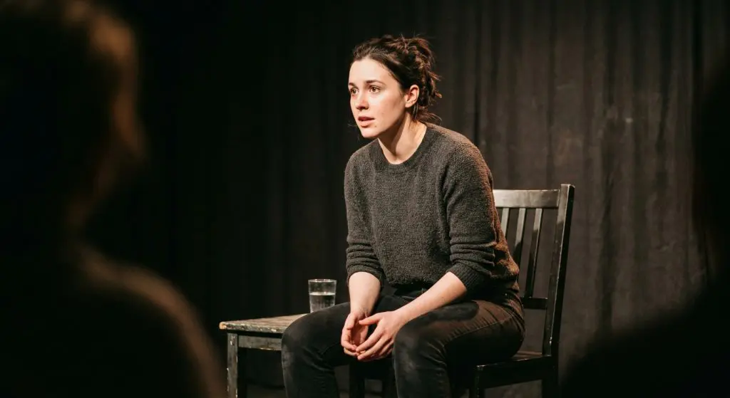 Actress performing a monologue seated under a single stage light