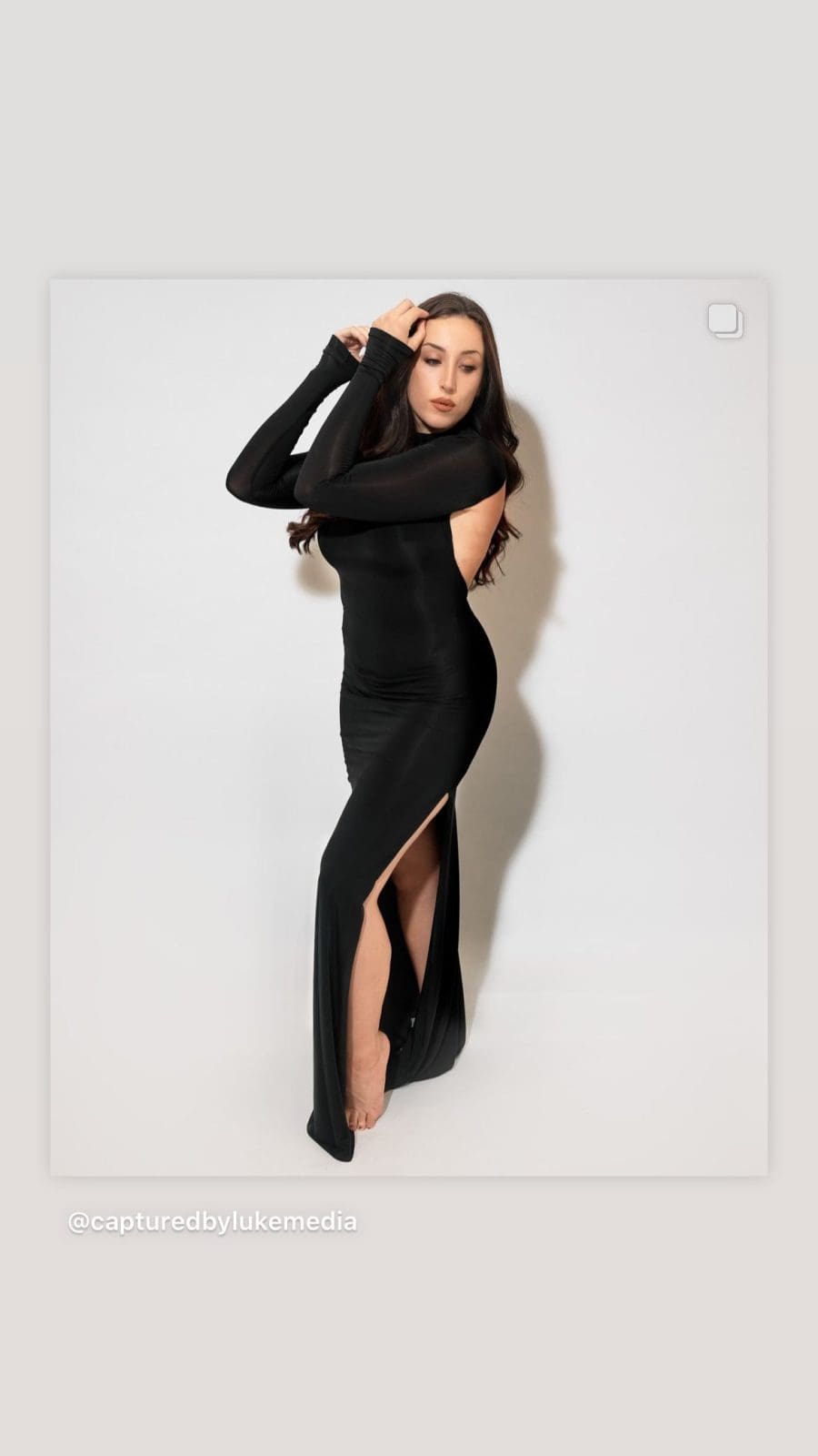 Content creator in a long black dress on a white studio backdrop, shown on a phone screen