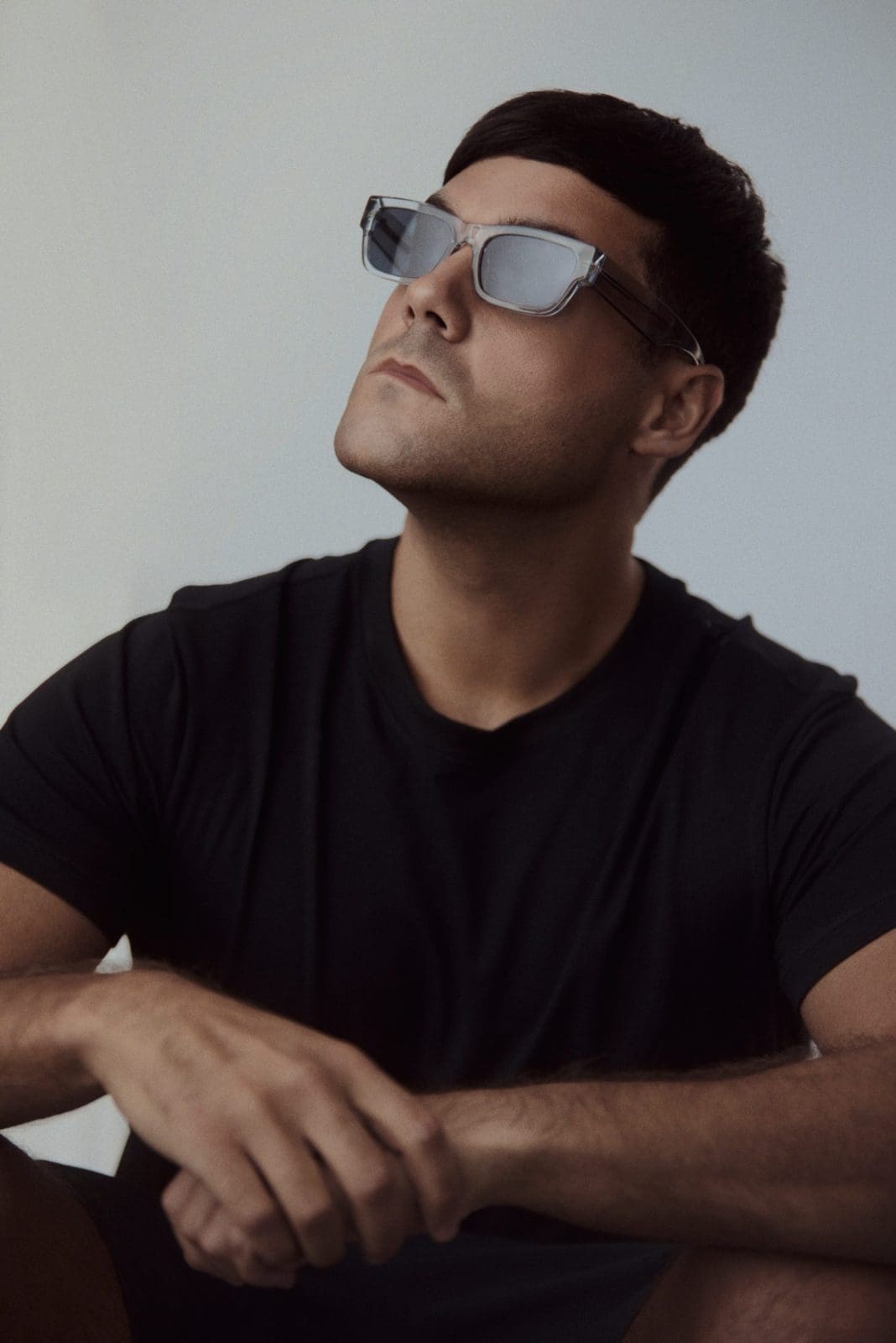 Music artist in sunglasses and a black t-shirt seated against a soft grey backdrop