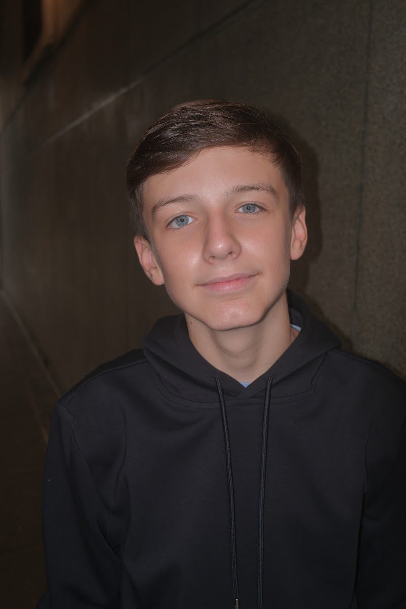Young actor in a navy hoodie with a soft smile, studio headshot on a dark background