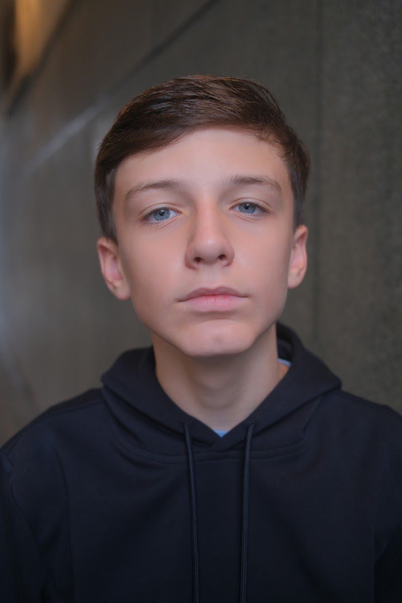 Young actor in a navy hoodie with a steady, serious look to camera, studio headshot
