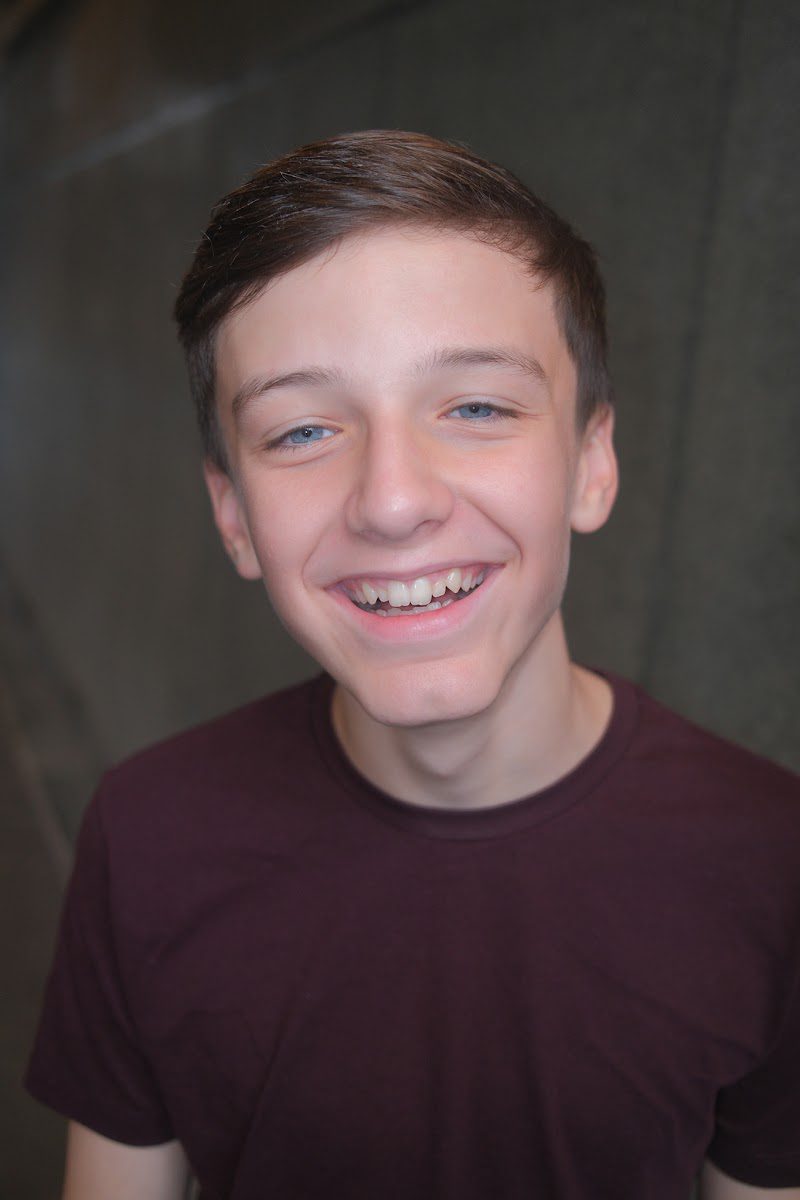 Young actor in a burgundy t-shirt with a wide, open smile, commercial style headshot