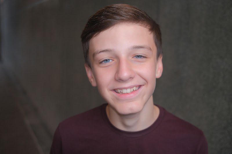 Landscape crop of a young actor in a burgundy t-shirt smiling, studio headshot