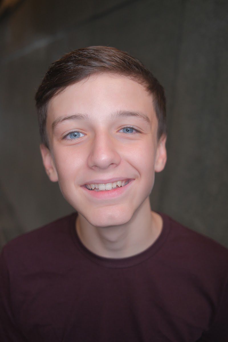 Young actor in a burgundy t-shirt with a friendly smile, eyes to camera