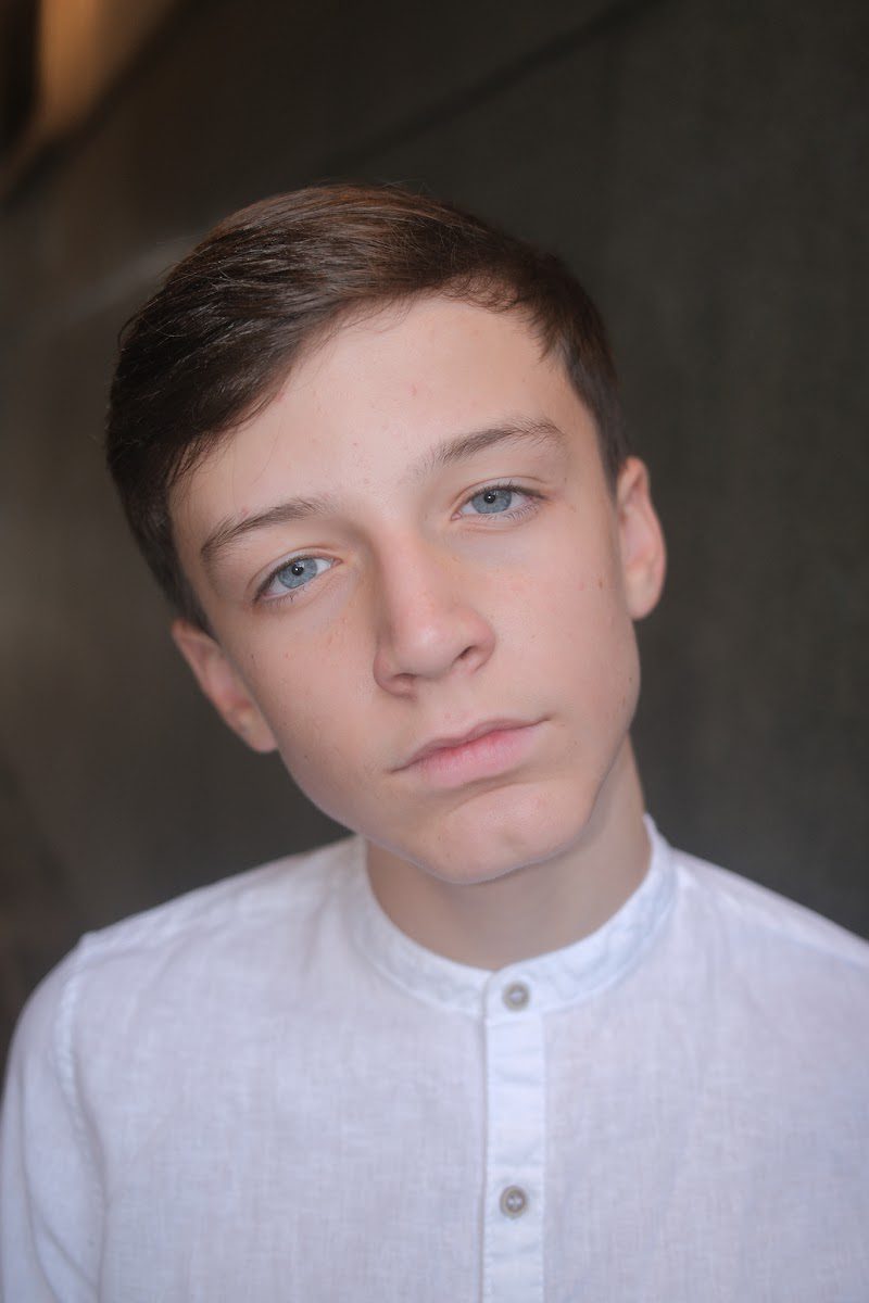 Young actor in a white collarless shirt, head tilted, serious theatrical headshot