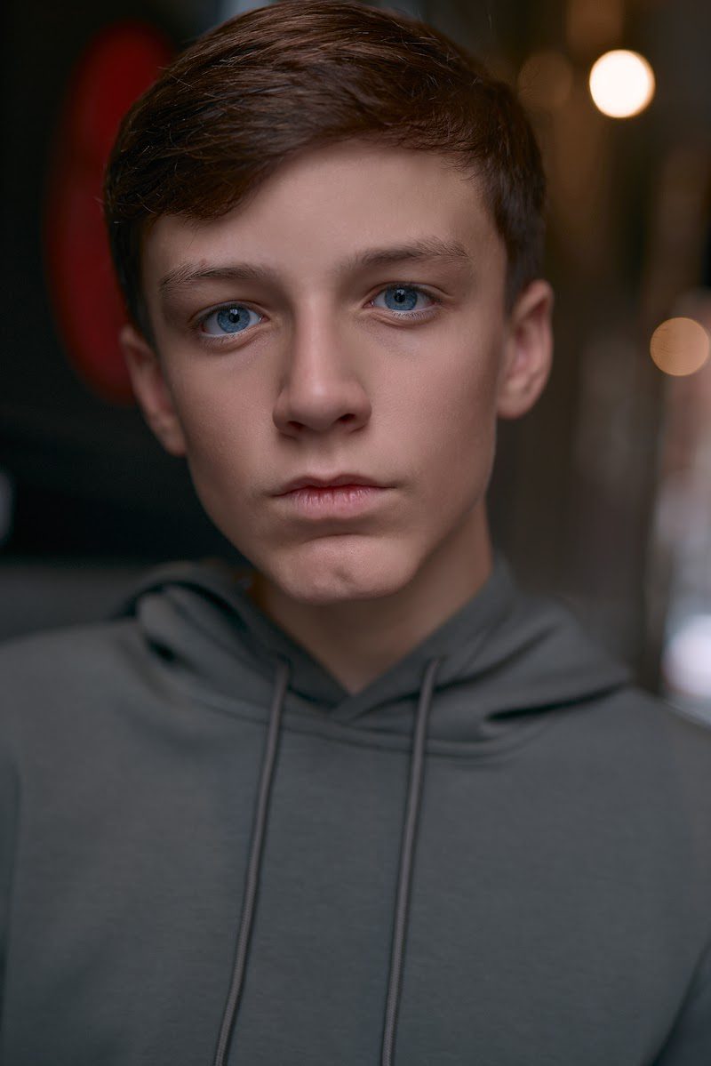 Young actor in a grey hoodie on location in Liverpool, serious and focused, bokeh lights in the background