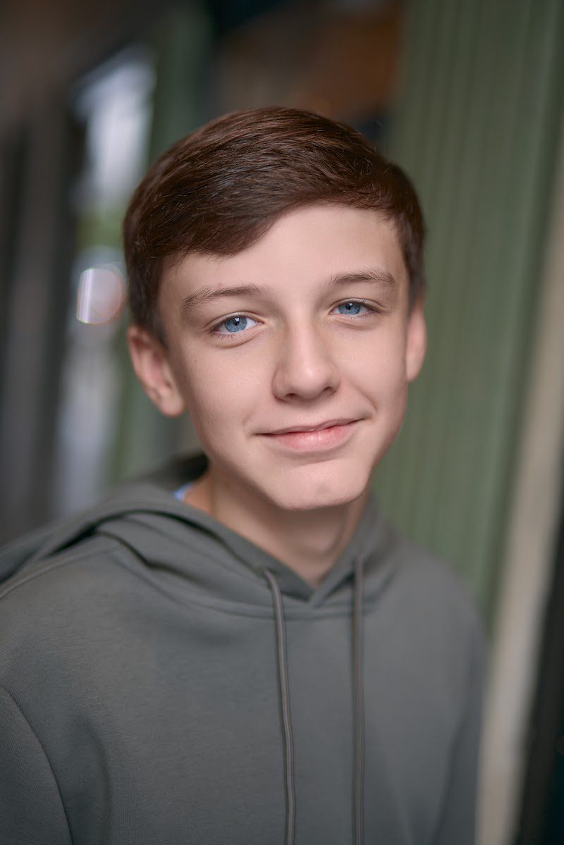 Young actor in a grey hoodie, gentle smile on location with a green backdrop
