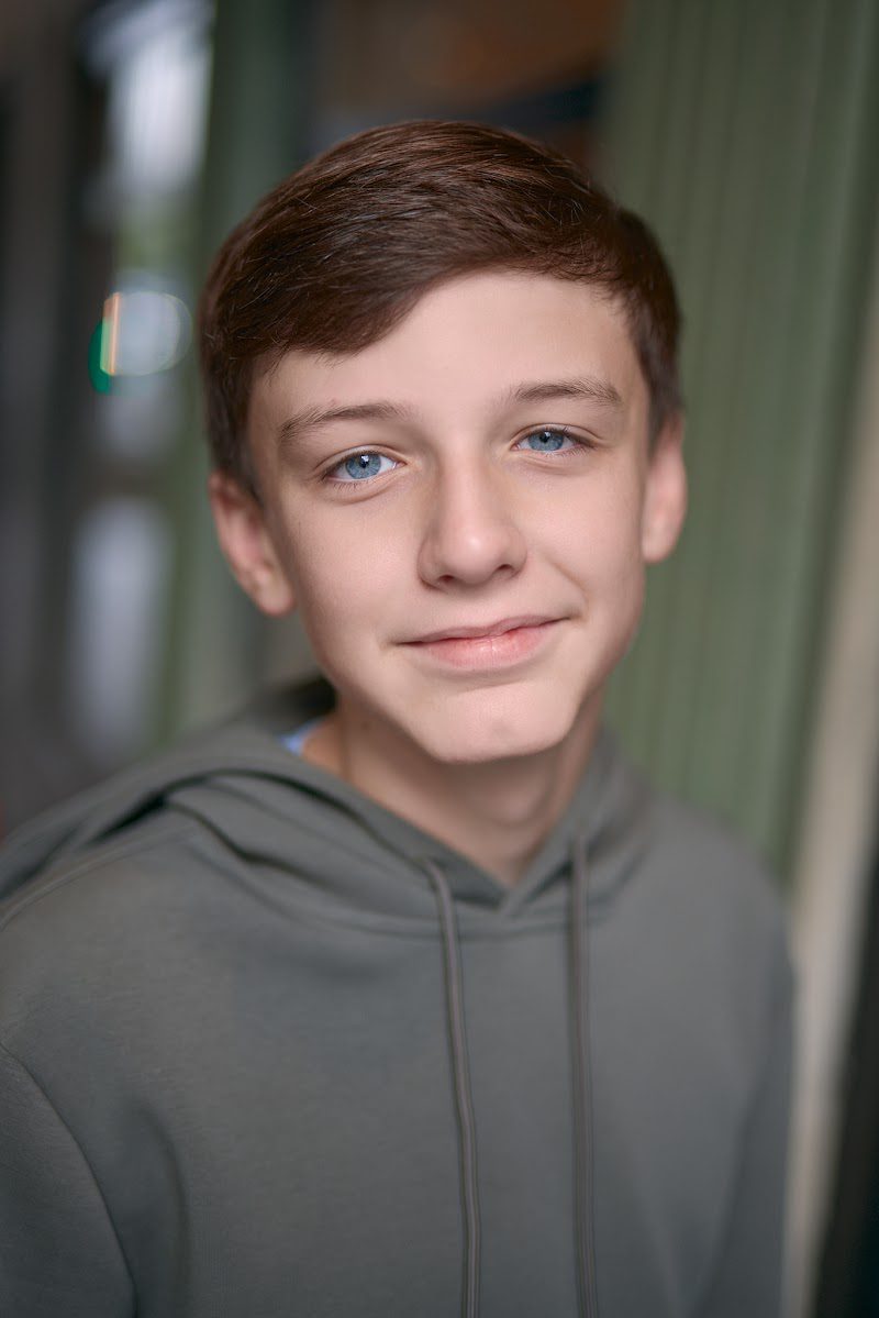Young actor in a grey hoodie, relaxed half smile on location