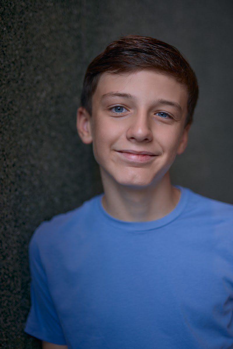Young actor in a bright blue t-shirt on a dark studio backdrop, soft smile