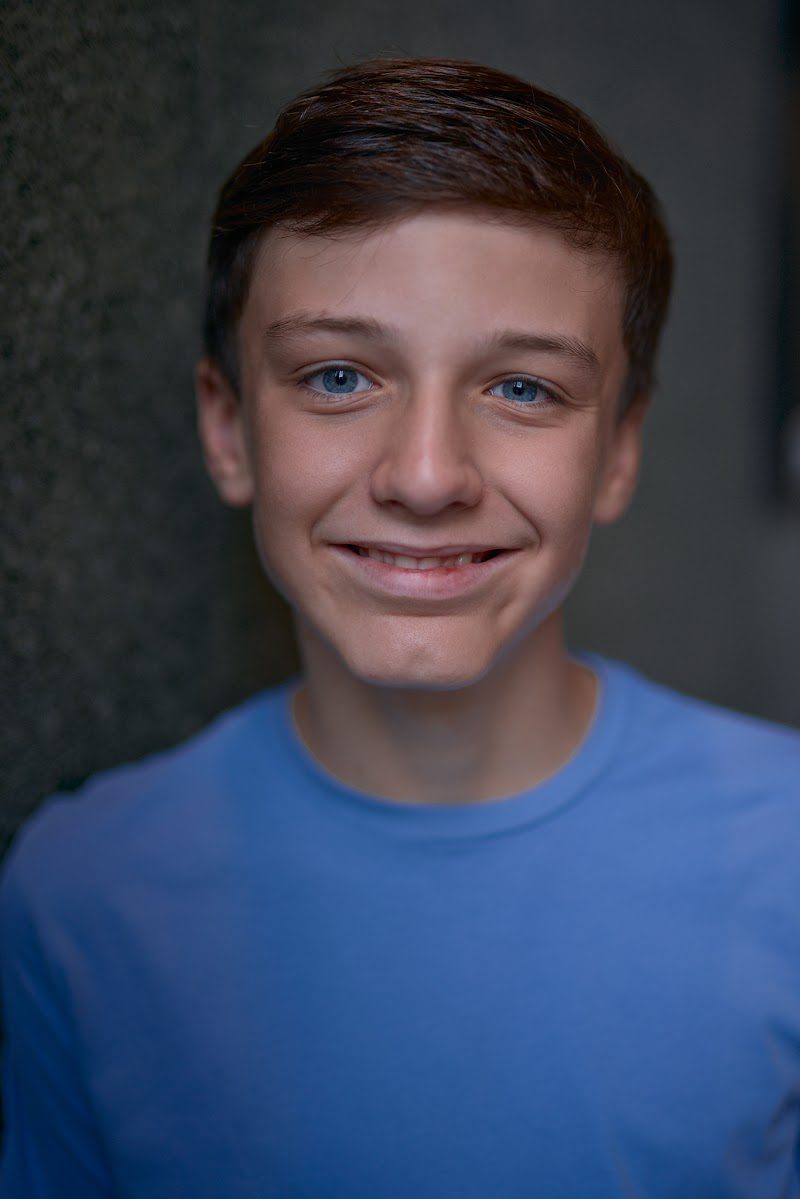 Young actor in a bright blue t-shirt on a dark studio backdrop, broad smile