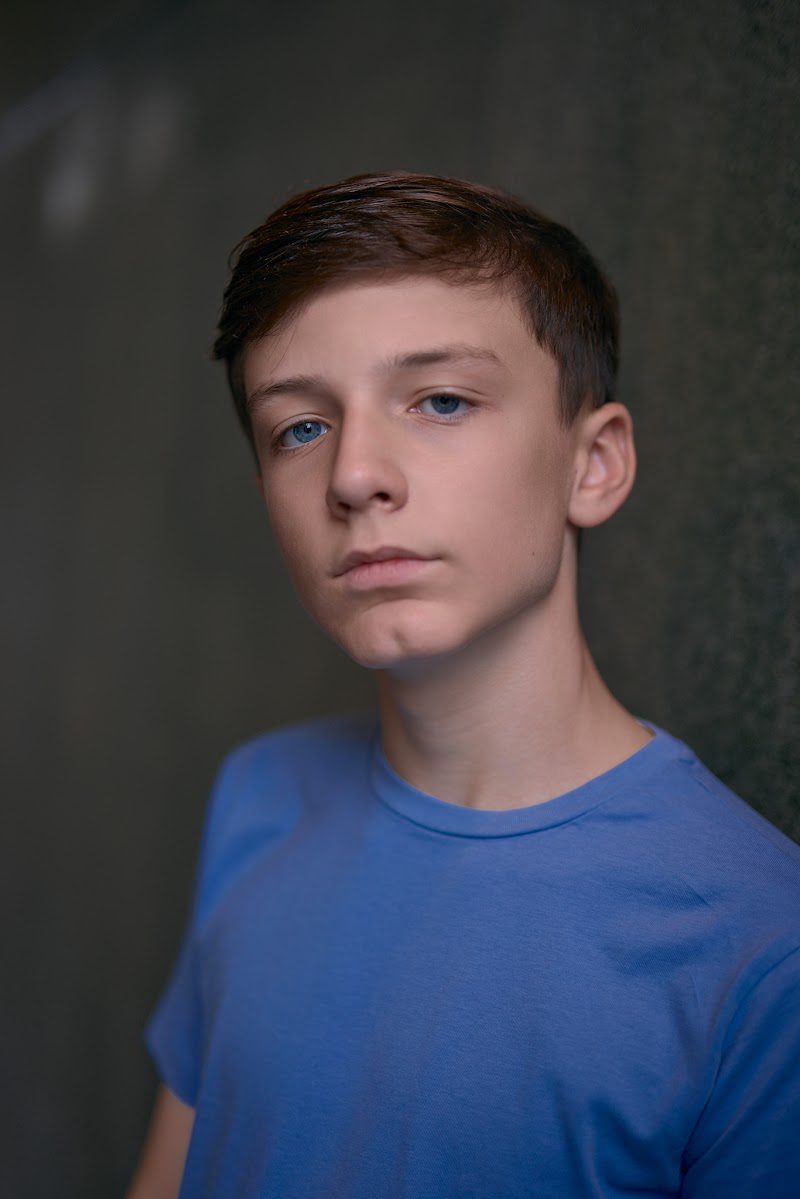 Young actor in a bright blue t-shirt on a dark studio backdrop, head tilted, serious look