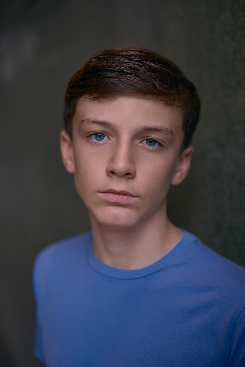 Young actor in a bright blue t-shirt on a dark studio backdrop, neutral expression