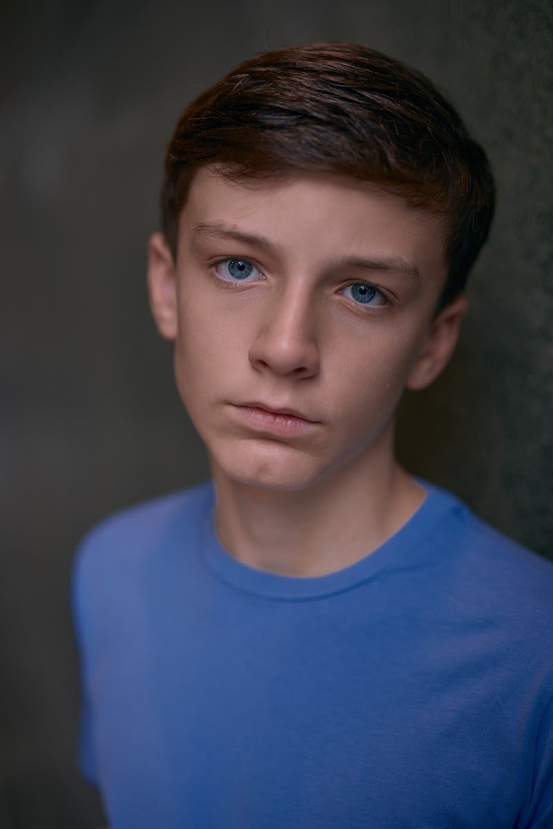 Young actor in a bright blue t-shirt on a dark studio backdrop, calm, straight to camera