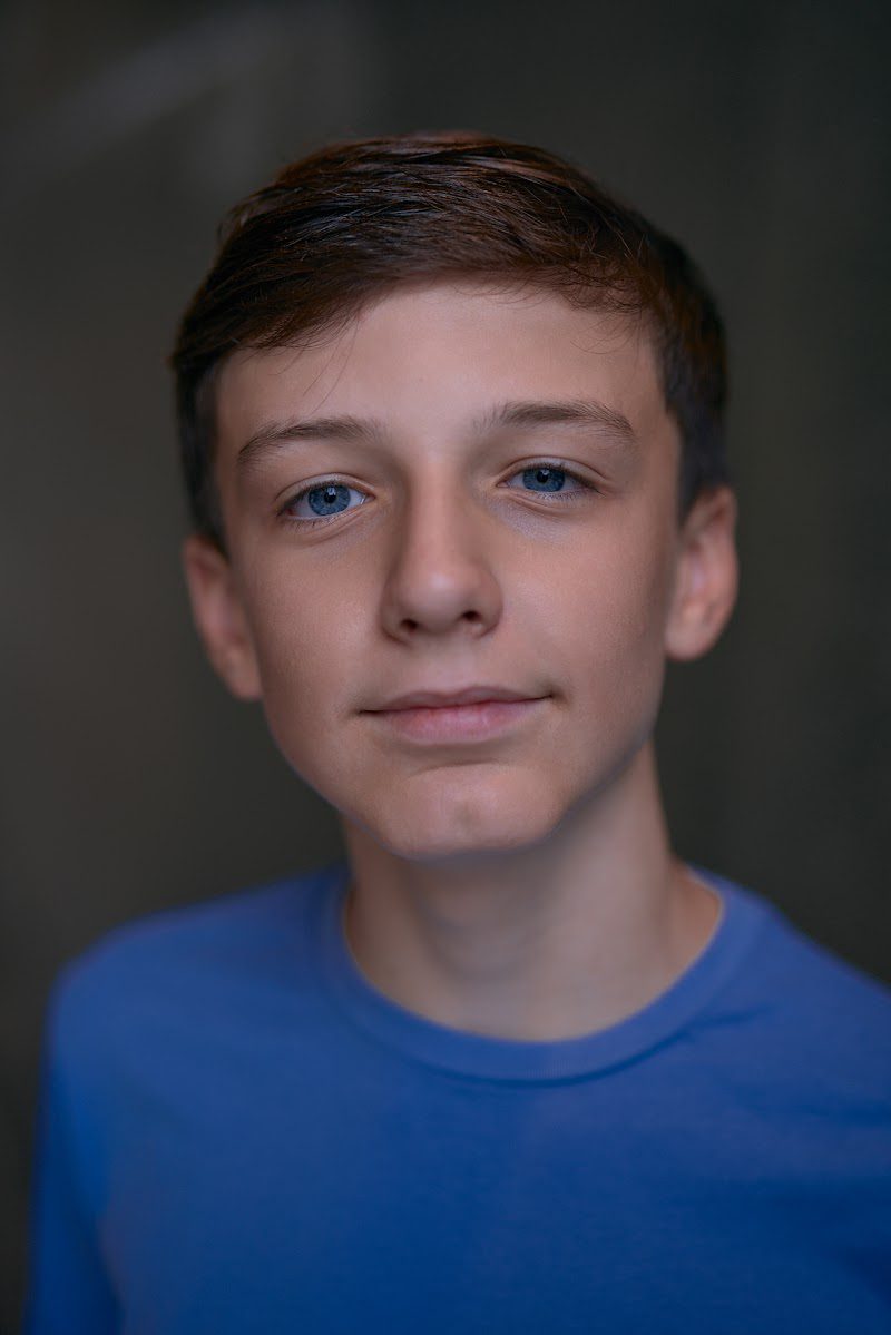 Young actor in a bright blue t-shirt on a dark studio backdrop, slight smile