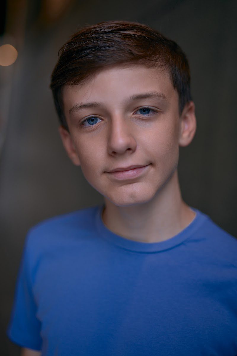 Young actor in a bright blue t-shirt on a dark studio backdrop, gentle smile