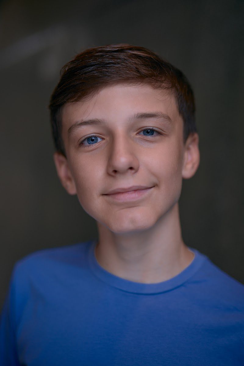 Young actor in a bright blue t-shirt on a dark studio backdrop, relaxed half smile