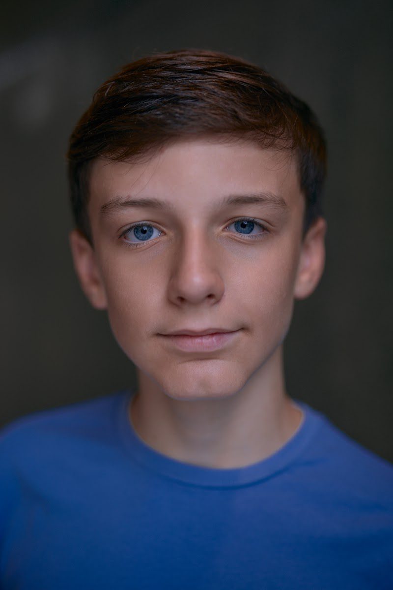 Young actor in a bright blue t-shirt on a dark studio backdrop, neutral, thoughtful look