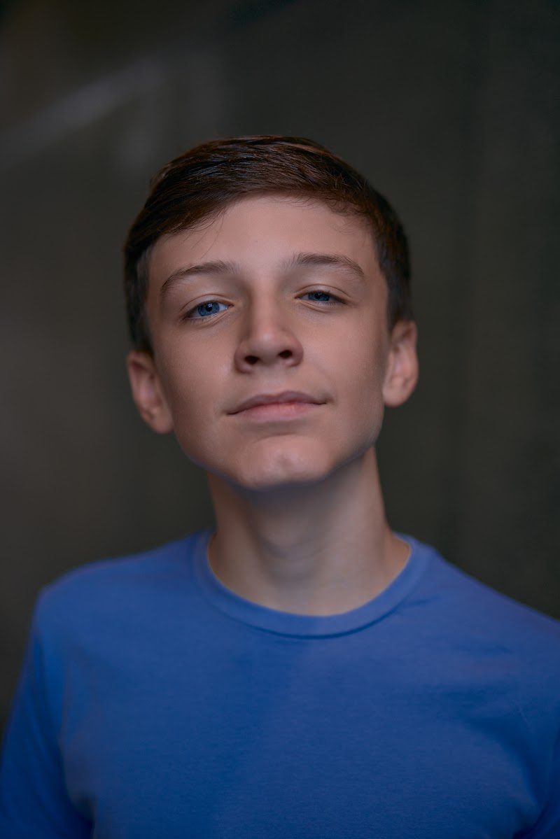 Young actor in a bright blue t-shirt on a dark studio backdrop, chin raised, serious expression
