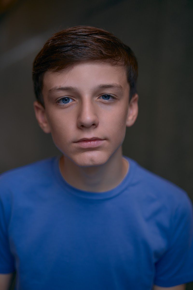 Young actor in a bright blue t-shirt on a dark studio backdrop, steady neutral look