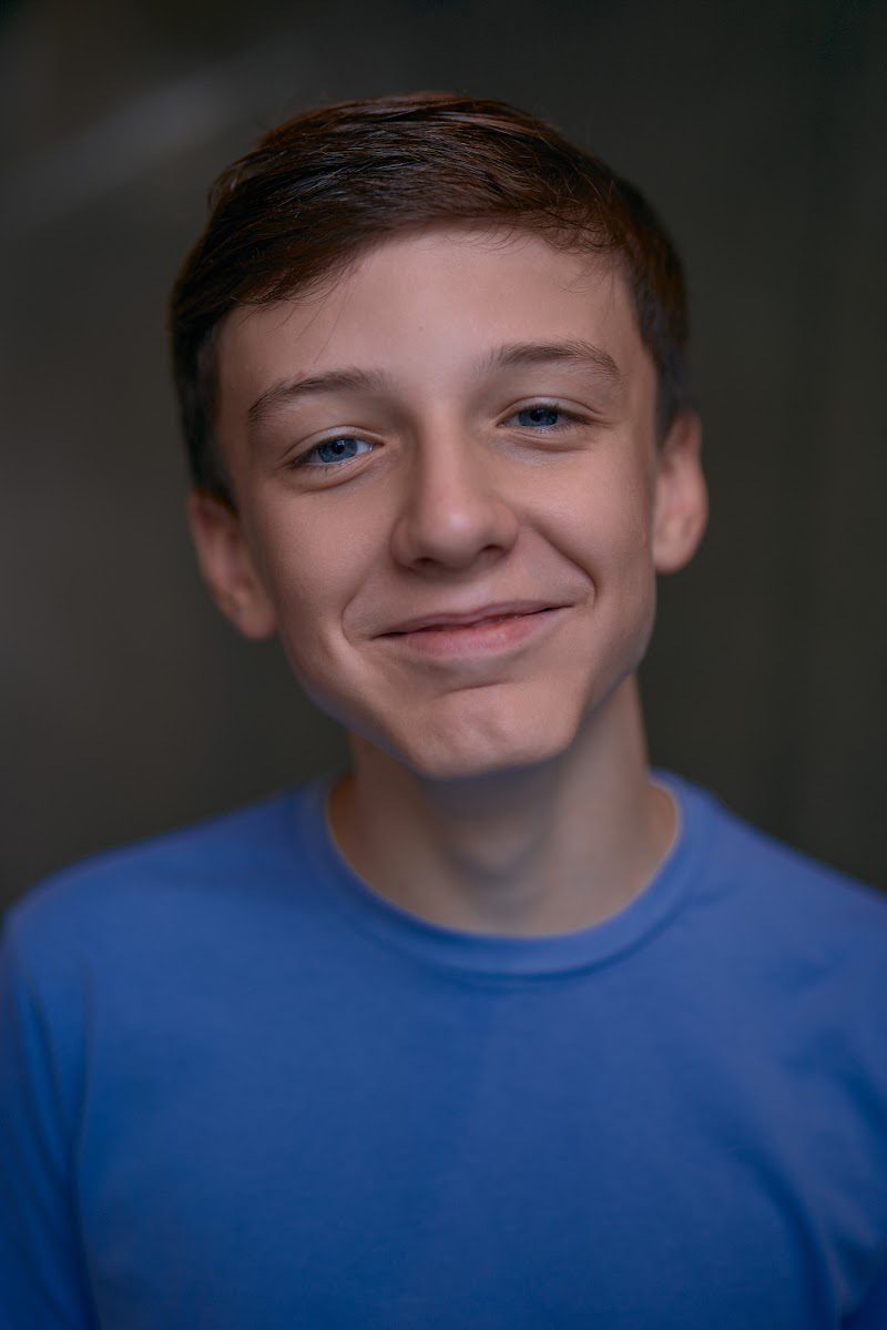 Young actor in a bright blue t-shirt on a dark studio backdrop, warm smile
