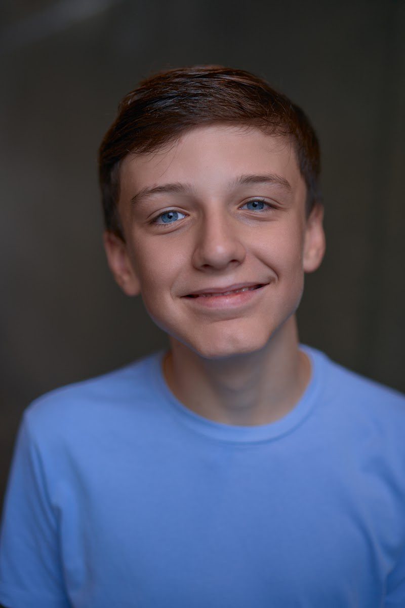 Young actor in a bright blue t-shirt on a dark studio backdrop, soft smile, slight head tilt