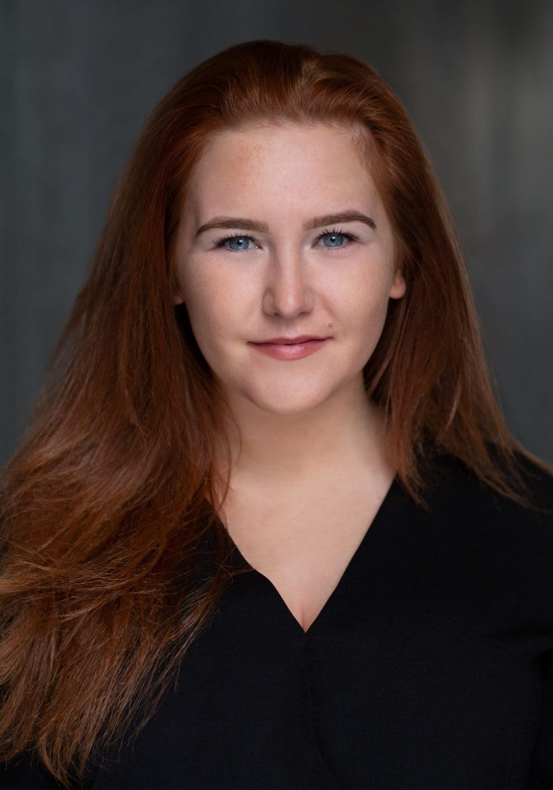 Headshot of a red-haired actress in a black shirt against a dark background