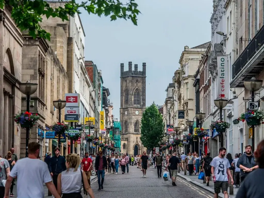 People walking down a busy Liverpool city centre street towards a church tower