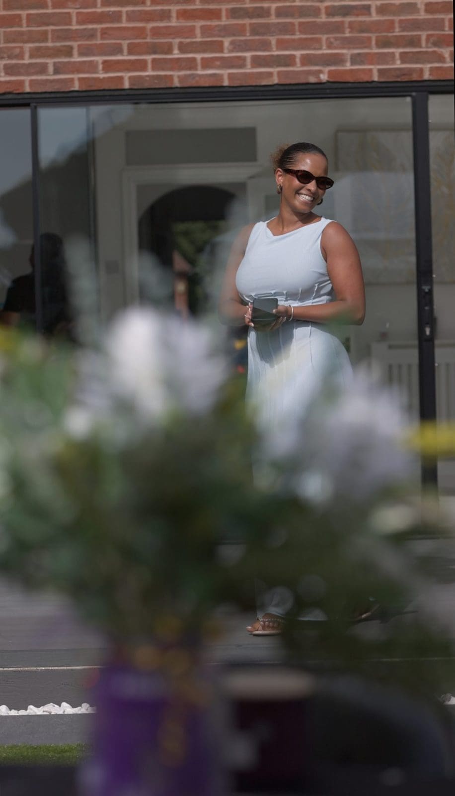 Woman in a white dress walking past a shopfront framed by flowers, lifestyle brand photo